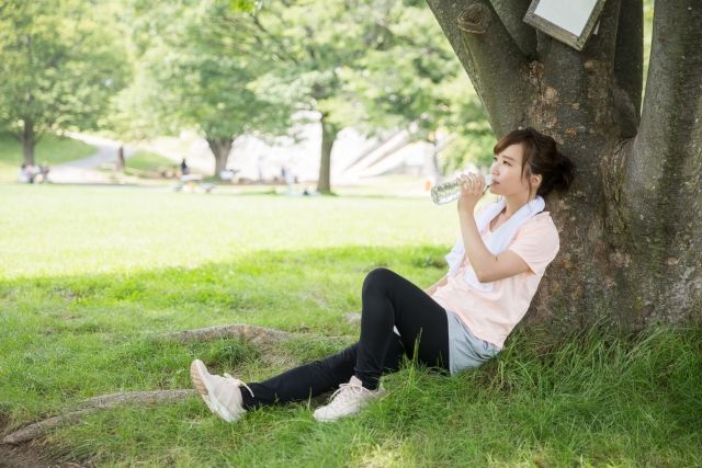 公園で水を飲んで一休みする女性