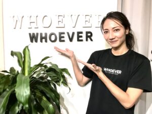 WHOEVERジムの看板まえで看板をアピールする女性